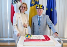 Landeshauptfrau Johanna Mikl-Leitner mit Gunnar Prokop, der zum 85. Geburtstag auch eine Geburtstagstorte sowie – als passionierter Radfahrer – auch einen blau-gelben Fahrradhelm überreicht bekam.