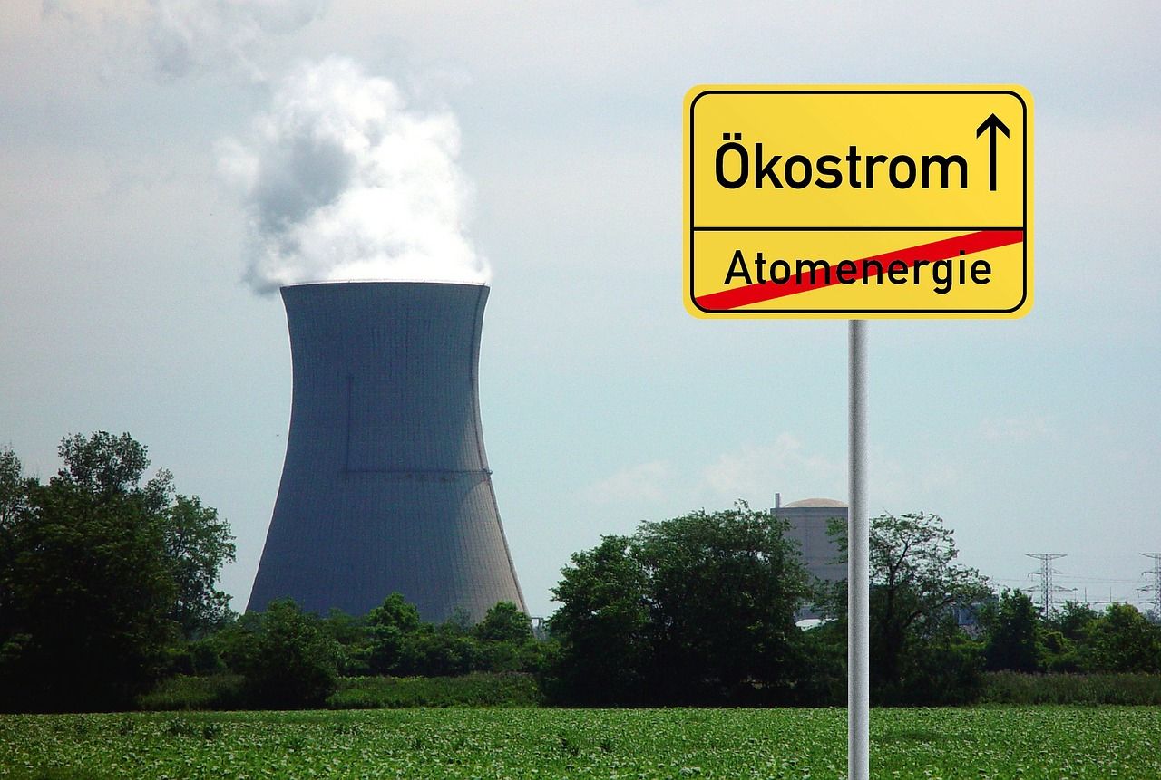 dampfender Atommeiler, davor Schild mit einem Richtungspfeil zu Ökostrom